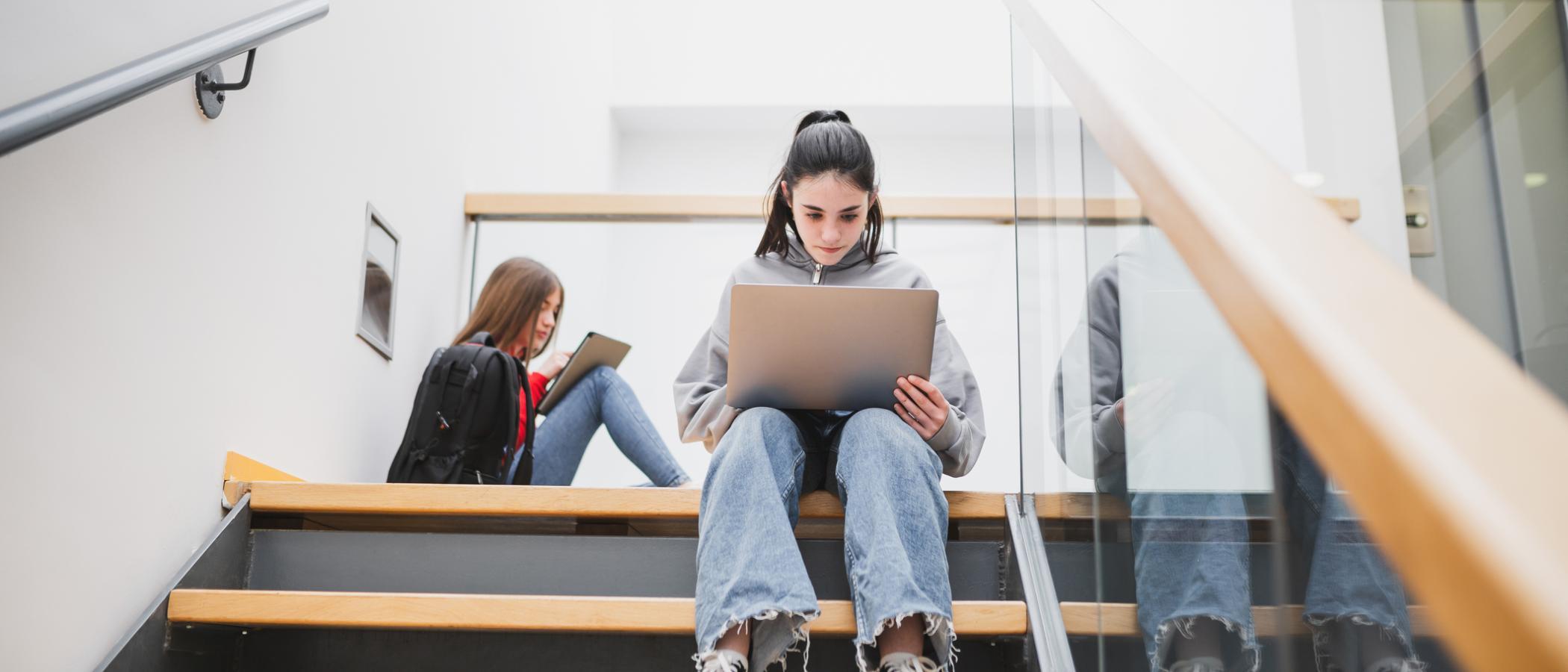 Eine Schülerin sitzt mit einem Laptop auf einer Treppe in der Schule