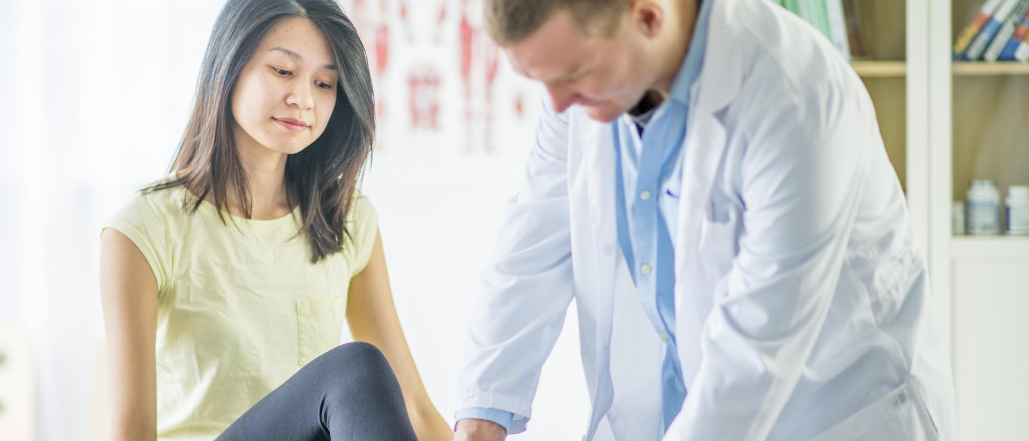 Eine junge Frau lässt sich von einem Arzt den Knöchel untersuchen.