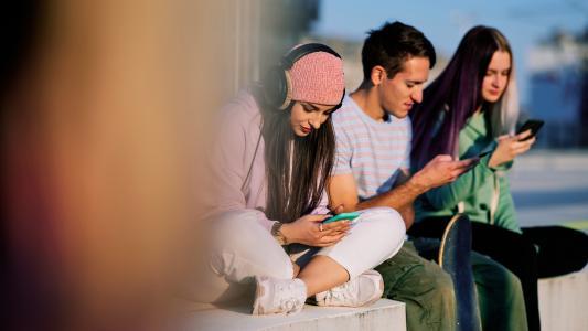 Drei Teenager sitzen nebeneinander, jeder schaut auf sein eigenes Handy
