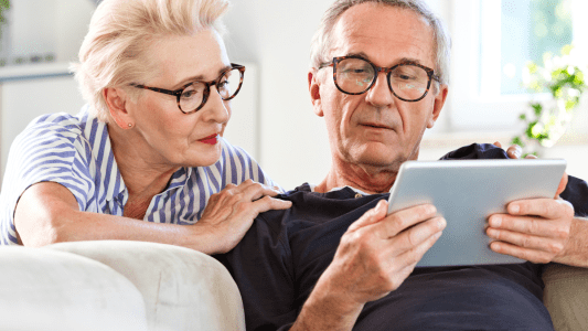 Älteres Ehepaar sitzt mit Tablet auf der Couch