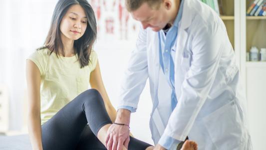 Eine junge Frau lässt sich von einem Arzt den Knöchel untersuchen.